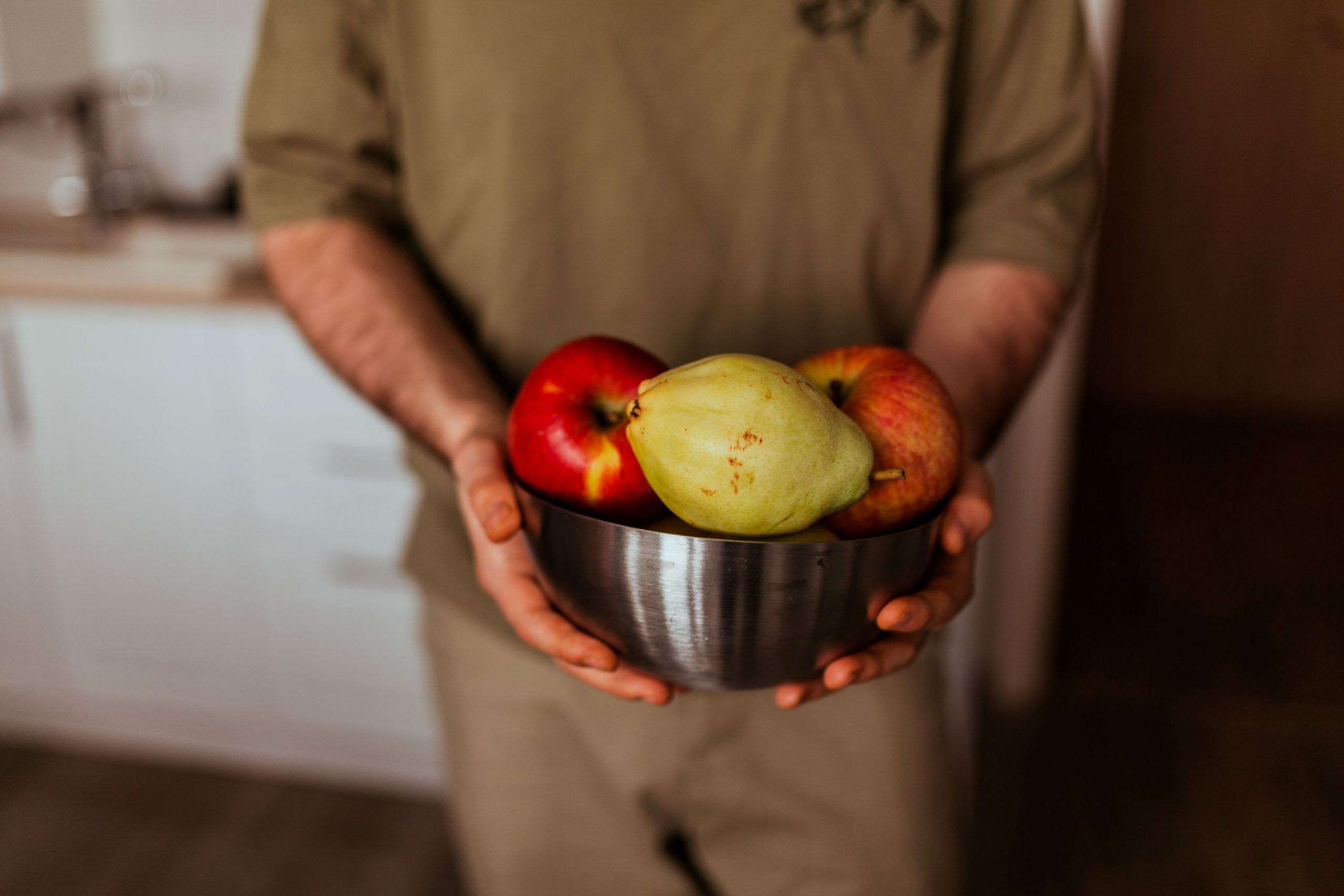 uomo che proge una scodella di frutta fresca con pere e mele da mangiare dopocena